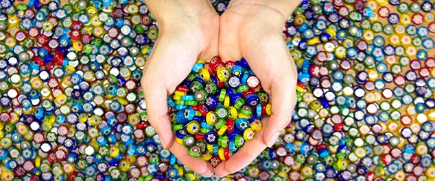 Hands holding a pile of millerfiori gems in assorted colors for use in mosaic art.